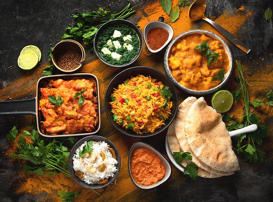 A variety of indian food in bowls on a dark background.