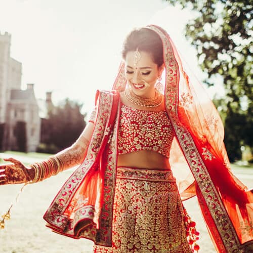 An indian bride in a red lehenga posing in front of a castle.