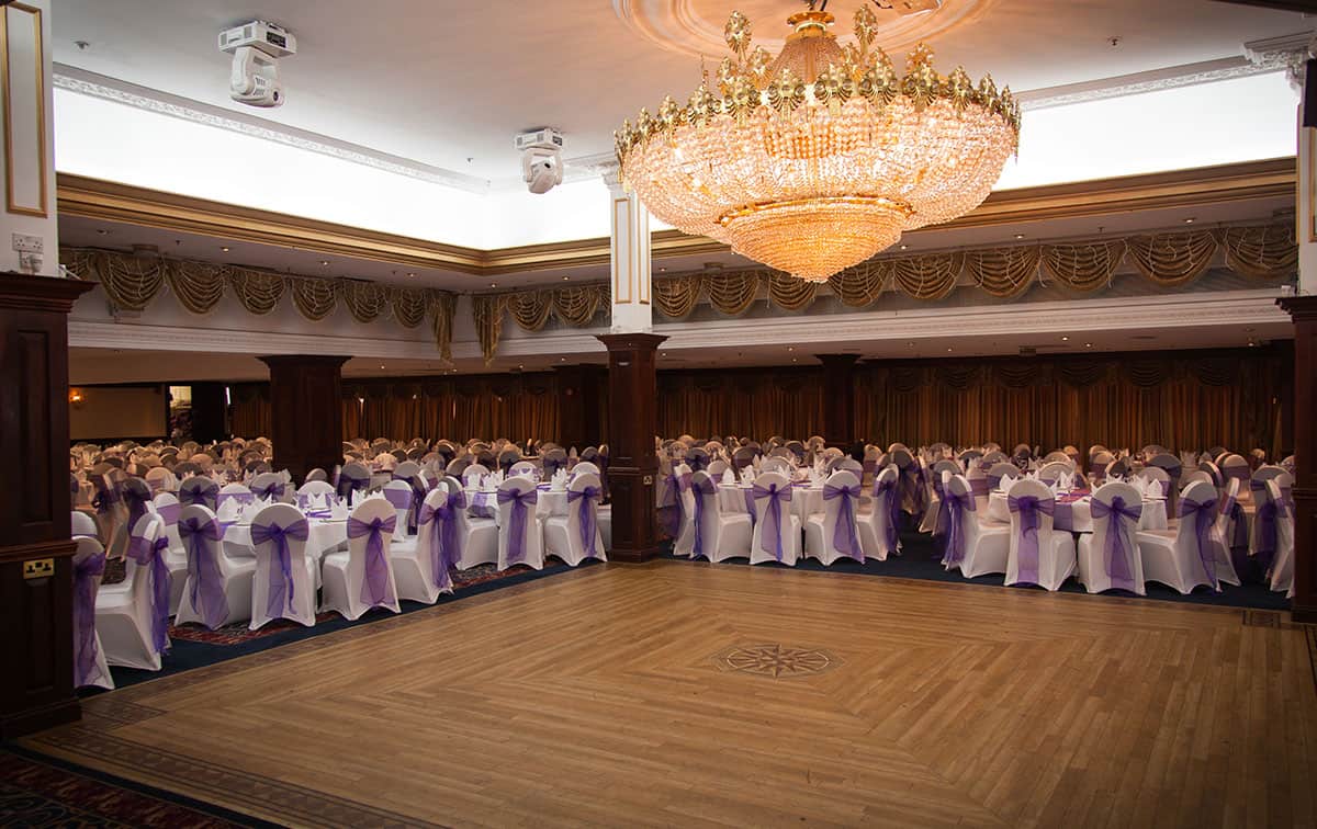 A large ballroom decorated with purple and white linens.