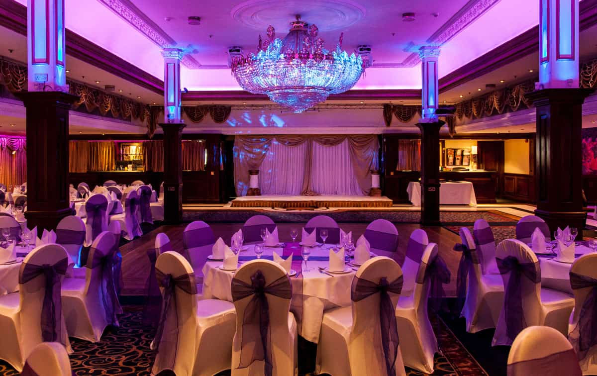 A banquet room with purple lights and white tablecloths.