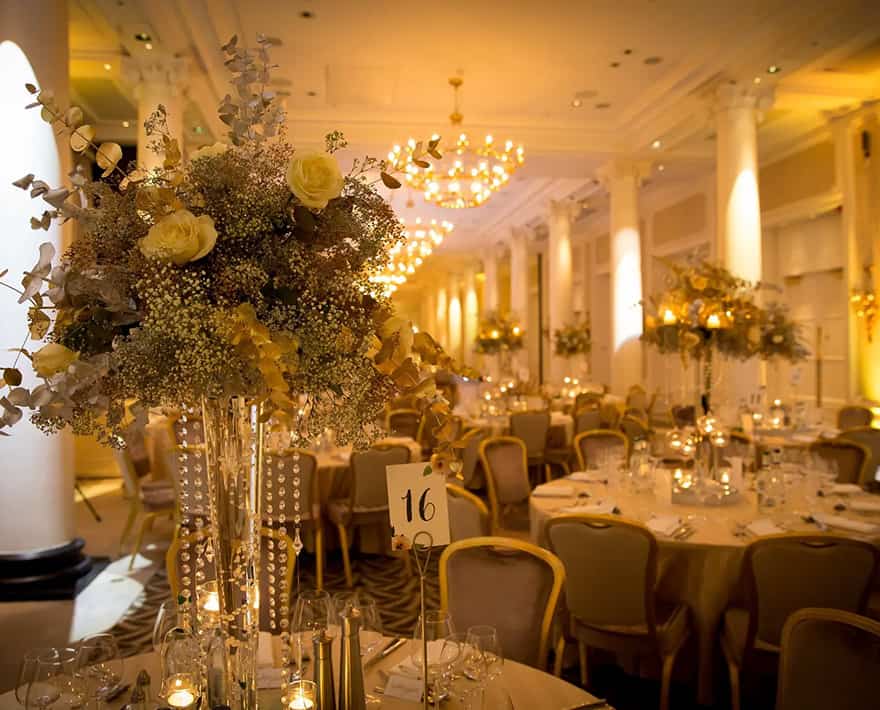 A large ballroom at the Waldorf Hilton hotel decorated with gold and white flowers.