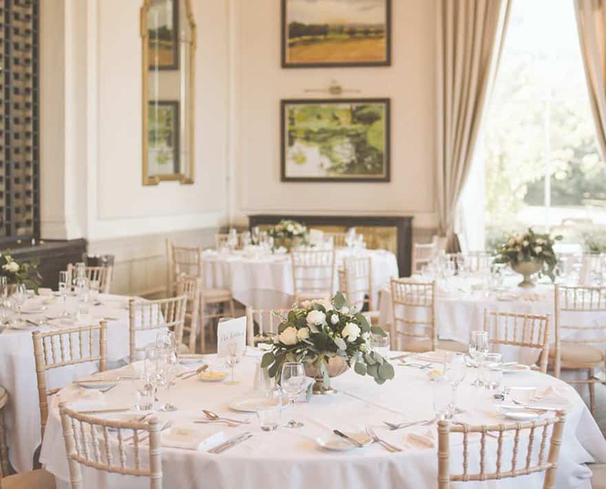 A wedding reception at Oatlands Park Hotel, with white tables and chairs set up in a spacious room.